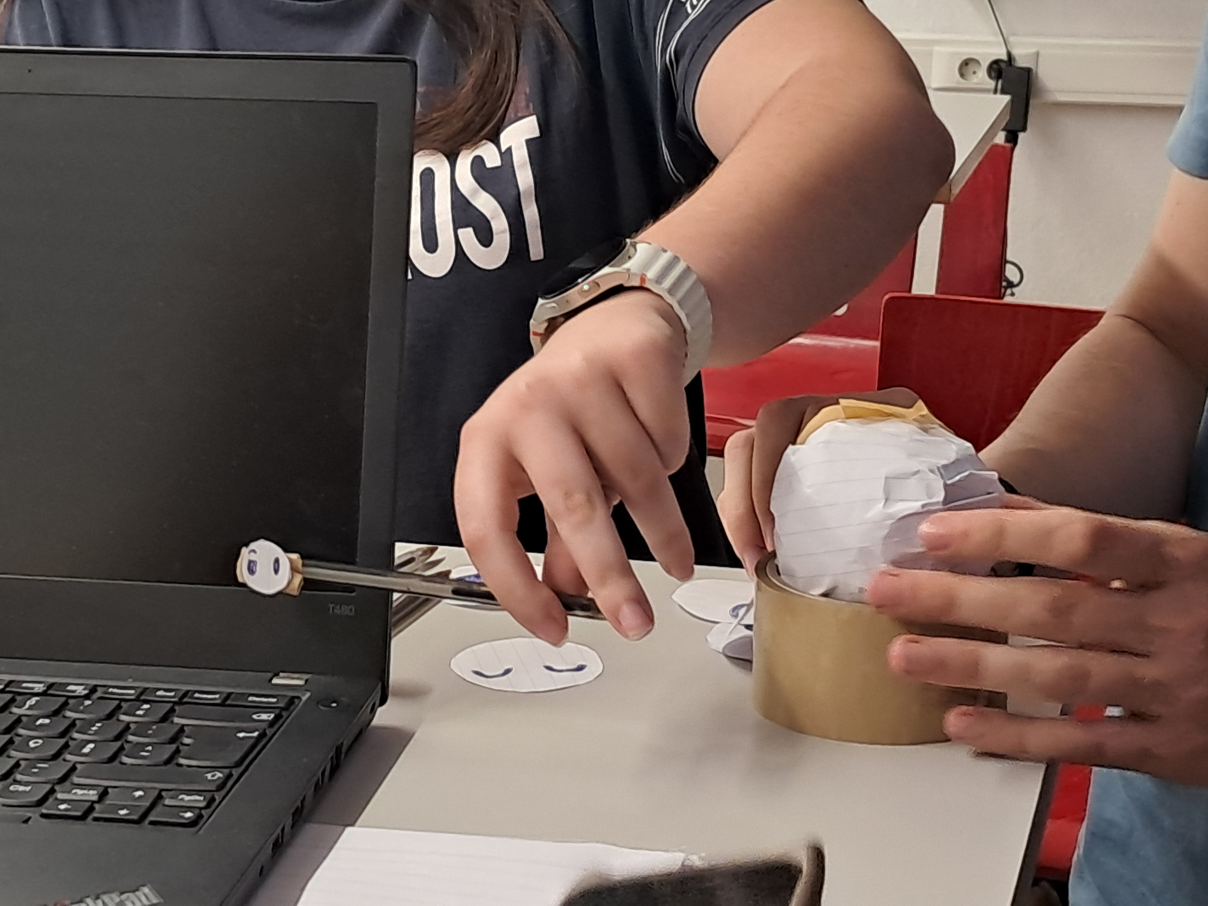 The co-designer tests the paper robot prototype beside a laptop.